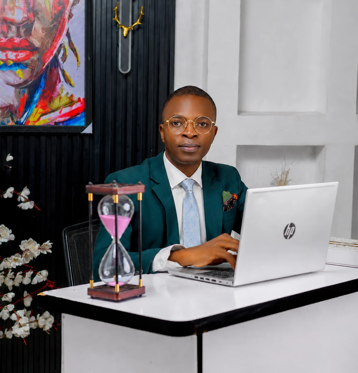 Pastor Folorunso Alesinloye seated in executive working context with laptop and hourglass